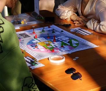 Twee mensen spelen een kleurrijk bordspel op een houten tafel, die baadt in warm zonlicht.